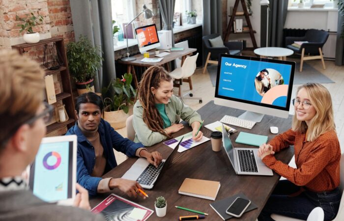 Team of diverse colleagues collaborating on project in modern office with digital devices and charts.