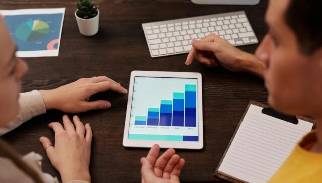 Team members discussing digital graphs on a tablet in a modern office setting.