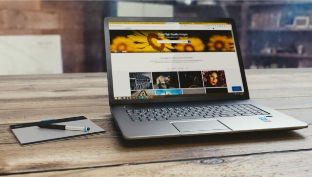 Laptop with open webpage on wooden desk, accompanied by tablet and pen, representing digital work setup.