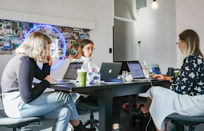 3 women sitting on chair in front of table with laptop computers