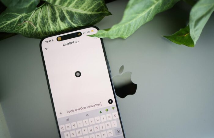 A smartphone shows a ChatGPT interface placed on an Apple laptop in a leafy environment.