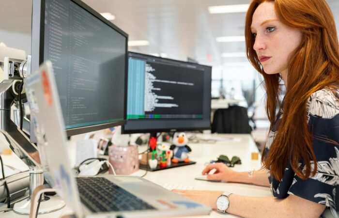A focused female software engineer coding on dual monitors in a modern office.