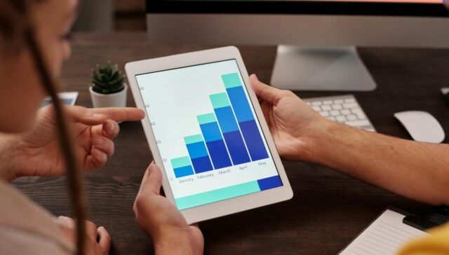 Two adults working in an office, examining graphs on a tablet screen for data analysis.