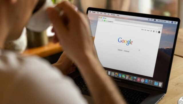 Close-up of an adult drinking coffee and browsing Google on a laptop indoors.