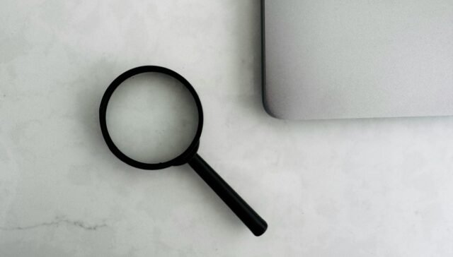 Magnifying glass sits near a laptop on a table.